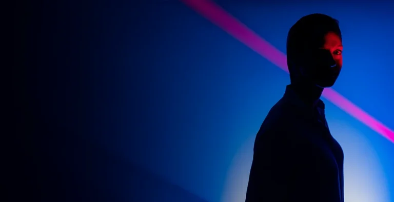 Silhouette einer Person vor blauem Hintergrund mit pinkem Lichtstrahl – symbolisiert digitales Wohlbefinden und moderne Technologie.